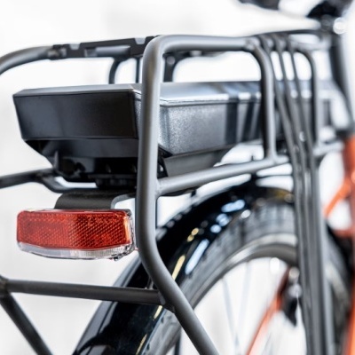 Bateria preta e refletor vermelho na parte traseira de bicicleta laranja com estrutura metálica preta