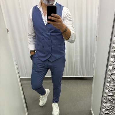 Homem com colete e calças azuis e camisa branca a tirar foto no espelho