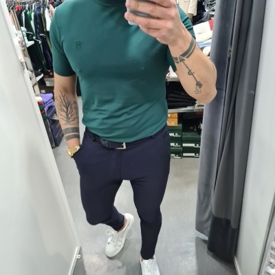 Homem com t-shirt verde escura e calças azul-escuras em prova num espelho