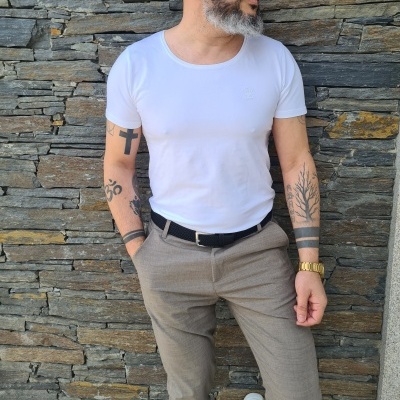 Homem com camiseta branca e calças castanhas contra muro de pedras