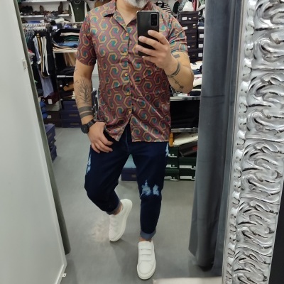 Homem com camisa colorida e calças rasgadas a tirar selfie numa loja