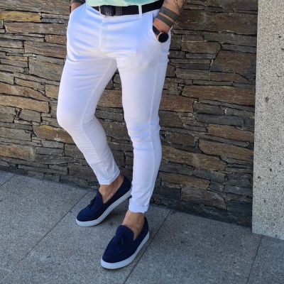 Homem com calças brancas e sapatos azuis diante de parede de pedra