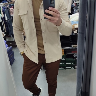 Homem com casaco bege e calças castanhas numa loja de roupas