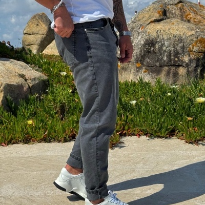 Calças de ganga cinza com ténis brancos ao ar livre com rochas e plantas ao fundo