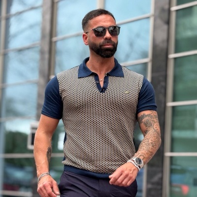 Homem com camisa pólo de malha estampada e calças pretas a andar em frente a edifício moderno de vidro