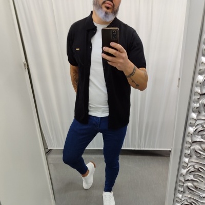 Homem em provador com camisa preta, t-shirt branca, calças azuis e sapatilhas brancas