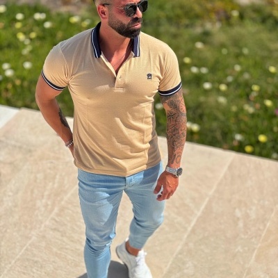 Homem com polo bege, calças de ganga azuis claras e ténis brancos em ambiente exterior