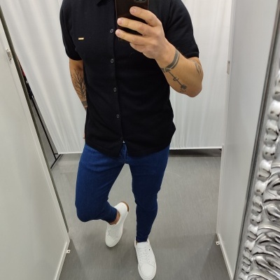 Homem com camisa preta, calças azuis e sapatilhas brancas a tirar selfie num espelho