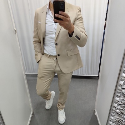 Homem com fato bege e camisa branca a tirar selfie em espelho interior