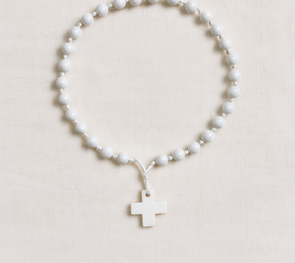 Terço branco com contas e cruz pendurada sobre tecido bege claro