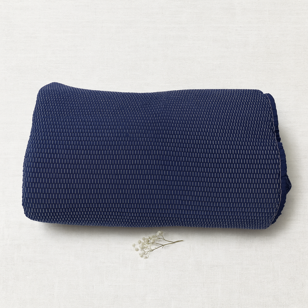 Manta azul escura dobrada com padrão texturizado e pequena flor branca ao lado