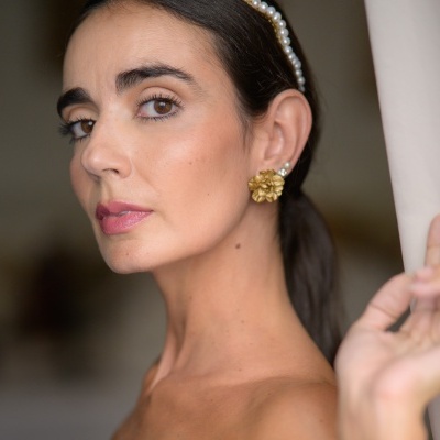 Mulher com brincos dourados de flor, pequenos brincos de pérola e bandolete de pérolas no cabelo