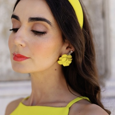 Mulher com vestido amarelo, banda de cabeça e brincos amarelos, maquilhagem suave, cabelo solto