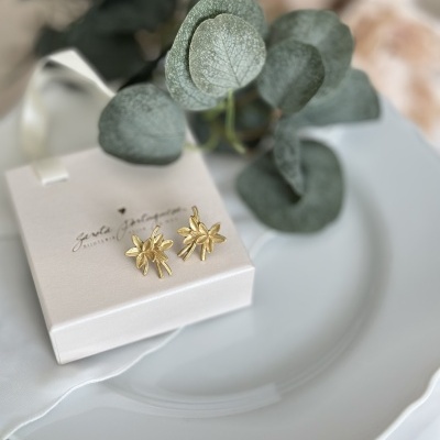 Brincos dourados flor em caixa branca sobre prato branco com folhas verdes