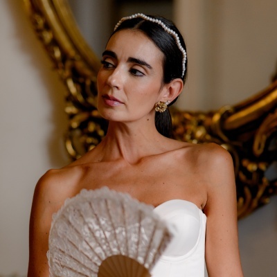 Mulher com vestido branco e leque rendado segurando, com acessórios dourados e pérolas