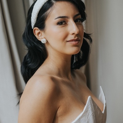 Mulher com vestido branco texturizado, faixa branca no cabelo e brincos redondos brancos