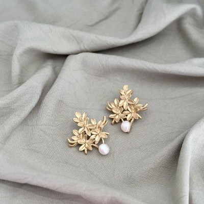 brincos dourados com flores e pérola em tecido cinzento claro
