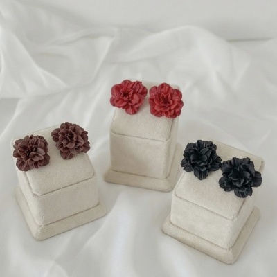 Brincos florais castanhos, vermelhos e pretos em suportes de veludo creme