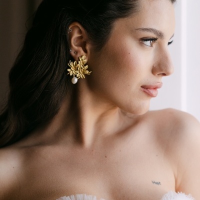 Mulher usa brincos dourados florais com pérola, vestindo roupa branca com tule