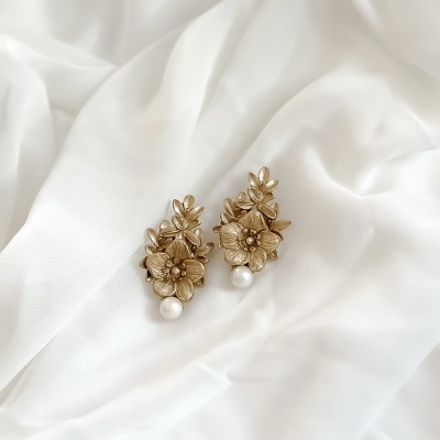 Brincos dourados com flores e pérola sobre tecido branco