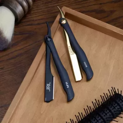 Três navalhas modernas em preto e dourado sobre tabuleiro de madeira clara com pincel de barbear e escova preta