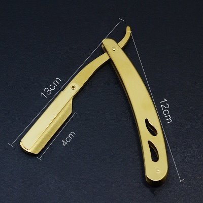 Navalha barbear dourada em metal com recortes decorativos sobre fundo preto.