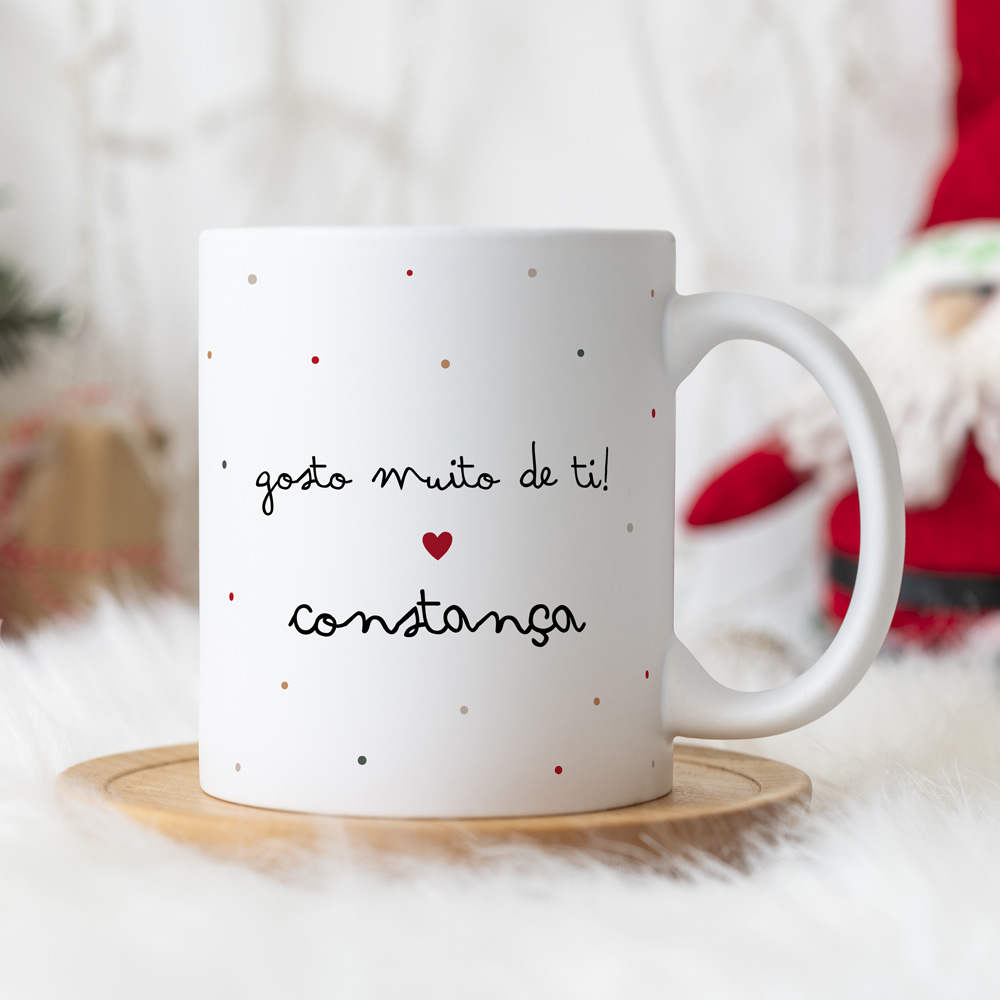 Caneca branca com pontos coloridos e texto em português, sobre prato de madeira em fundo de decoração natalícia.