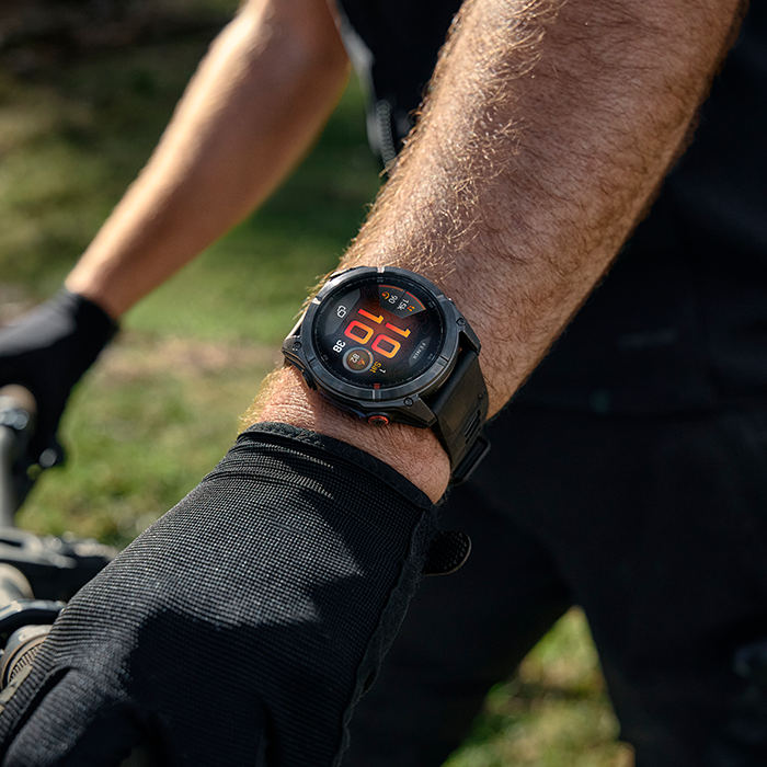 Relógio digital preto com bracelete preta no pulso de uma pessoa com luva preta.