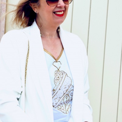 Mulher de blazer branco, camisola branca com padrão dourado, óculos de sol florais e batom vermelho