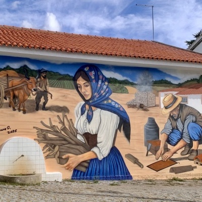 Mural de escena rural com mulher, homem e boi numa parede de casa com telhado de telha vermelha