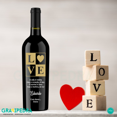 Garrafa de vinho com rótulo LOVE, cubos de madeira e coração vermelho ao lado.