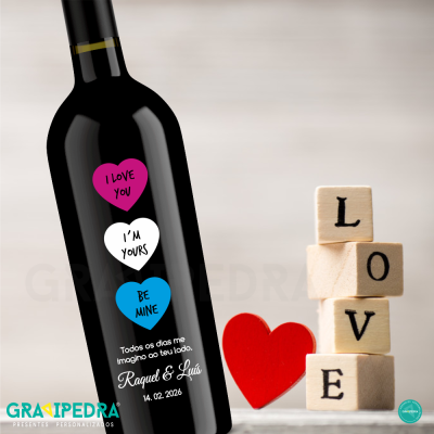 Garrafa de vinho personalizada com rótulo de corações coloridos e blocos de madeira formando a palavra LOVE ao lado.