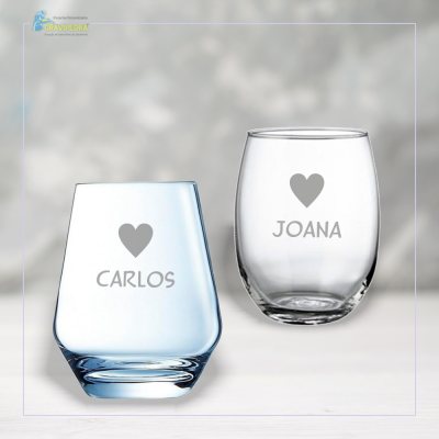 Dois copos gravados com nomes Carlos e Joana em fundo cinzento desfocado
