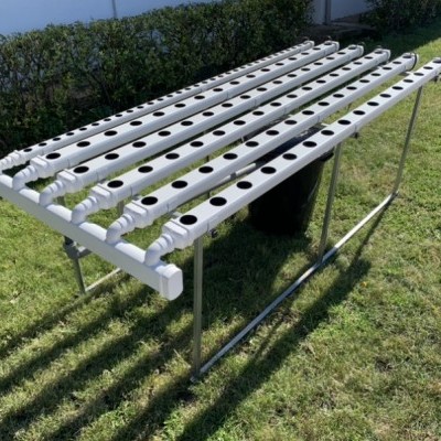Estrutura de cultivo hidropónico com tubos de PVC brancos e armação metálica sobre relvado