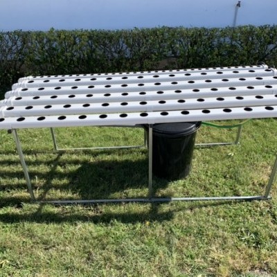 Estrutura metálica de cultivo hidropónico com canaletas brancas e orifícios para plantas no relvado