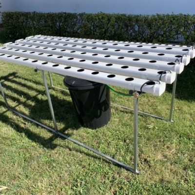 Estrutura metálica de hidroponia com tubos brancos perfurados em jardim