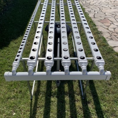 Sistema hidropónico com canais brancos e estrutura metálica na relva