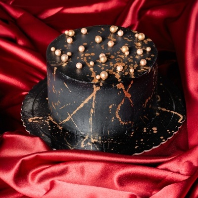 Bolo preto decorado com salpicos dourados e esferas douradas sobre tecido vermelho acetinado