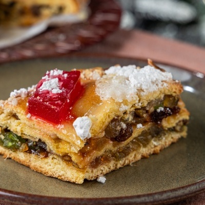 Fatia de bolo com frutas cristalizadas e açúcar em pó num prato castanho