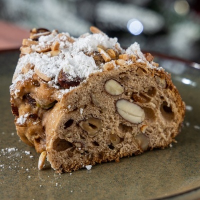 Pedaço de bolo com nozes e açúcar em pó num prato verde.