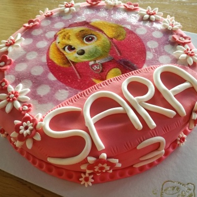 Bolo decorado rosa com flores e imagem de cão, texto SARA 2 em pasta branca
