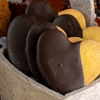 Bolachas de coração metade chocolate preto dentro de caixa cinzenta de tecido.