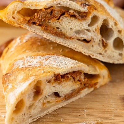 Pão recheado partido ao meio com recheio castanho sobre tábua de madeira.