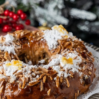 Bolo em forma de coroa com amêndoas, açúcar em pó e doce amarelo, sobre papel rendado e decoração natalícia