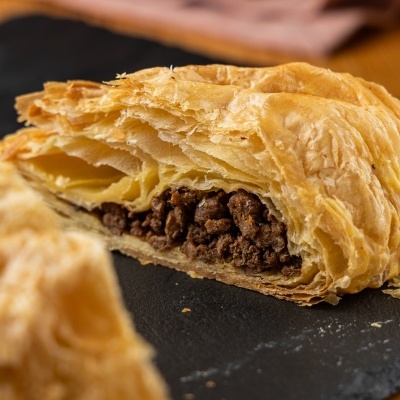 Pastel folhado recheado com carne picada em fundo escuro
