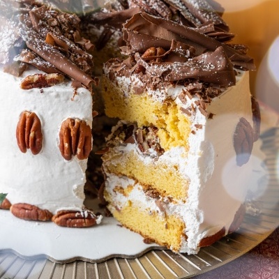 Bolo decorado com nozes pecans e chocolate, servido num prato dourado.