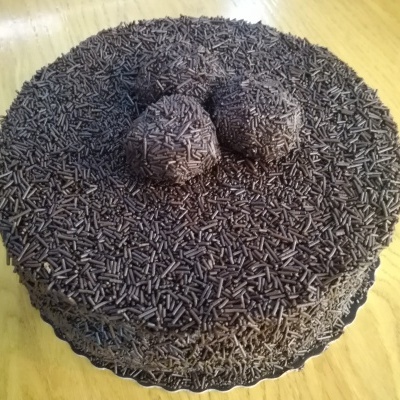 Bolo redondo coberto por granulado de chocolate com três brigadeiros no topo