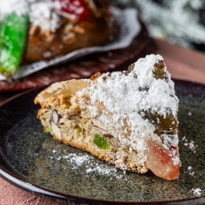 Fatia de bolo com frutos cristalizados e açúcar em pó num prato castanho escuro