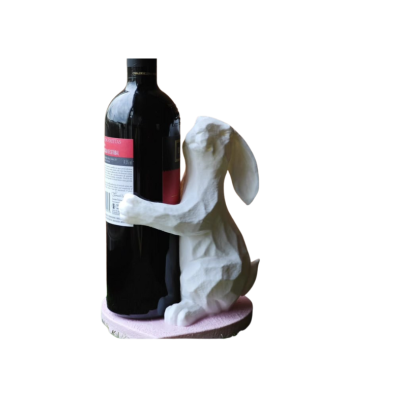 Estatueta branca de coelho ao lado de uma garrafa de vinho escura com rótulos vermelhos