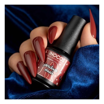 Frasco de verniz de unhas INOCOS vermelho escuro com mãos a segurar em fundo azul acetinado